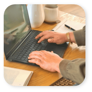 deux mains tapent sur le clavier d'un ordinateur postable posée sur un bureau en bois